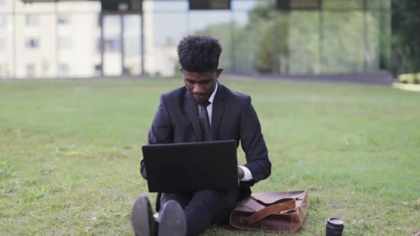 Aufgeregter Afrikaner mit Laptop, der vor dem Büro sitzt und die Arme hebt, um den Erfolg zu feiern — Stockvideo