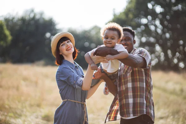 Hermosos padres multiculturales jugando con el hijo en el campo — Foto de Stock