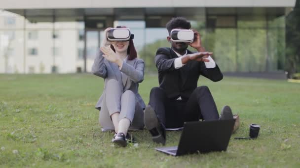 Πολυεθνικοί επιχειρηματίες, που κάθονται στο γρασίδι έξω από το γραφείο και δείχνουν στον αέρα με γυαλιά — Αρχείο Βίντεο