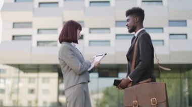 Beyaz kadın, ofis binasının yakınında el sıkışan Afrikalı Amerikalı erkek meslektaşını selamlıyor.