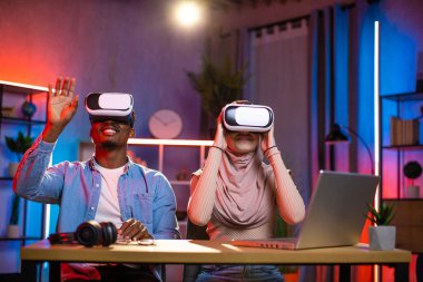 Çeşitli çiftler VR bardaklarıyla masada oturmuş oyun oynuyorlar.