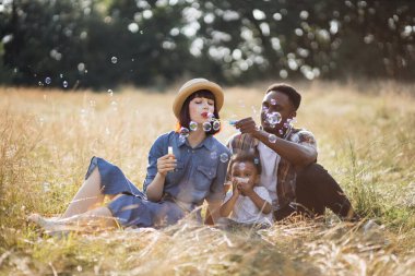 Karışık ırk ailesi temiz havaya sabun köpüğü üflüyor.
