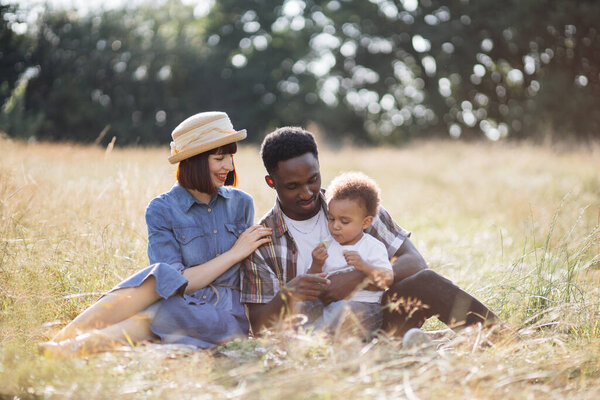 Multiracial parents and little son having picnic outdoors