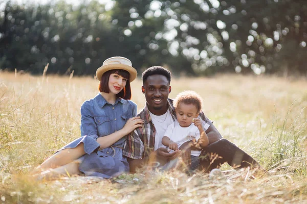 Multi família étnica de três sentados na grama durante o piquenique — Fotografia de Stock