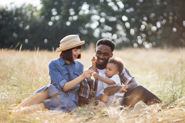 Felices padres de raza mixta con hijo comiendo uva en el picnic — Foto de Stock