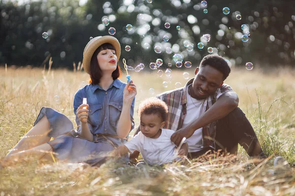 Multi pais étnicos com filho soprando bolhas de sabão ao ar livre — Fotografia de Stock