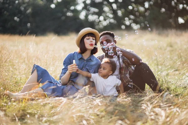 Pais multirraciais usando bolhas de sabão para brincar com o filho — Fotografia de Stock