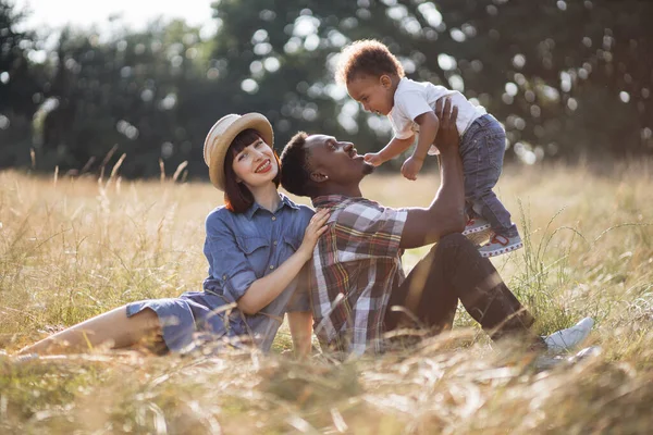 Pais multirraciais felizes brincando com o pequeno filho no campo — Fotografia de Stock