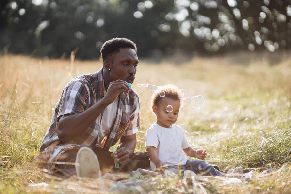 Pai africano soprando bolhas de sabão enquanto brincava com o filho — Fotografia de Stock