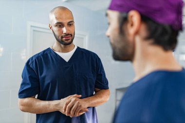 Two surgeons in scrubs converse in an operating room setting, likely discussing a medical procedure or patient care.