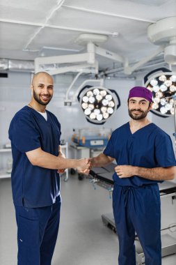 Two surgeons shake hands in a modern operating room, likely after a successful procedure or in agreement.