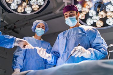 A surgical team is focused during an operation in a modern operating room, with bright lights overhead.