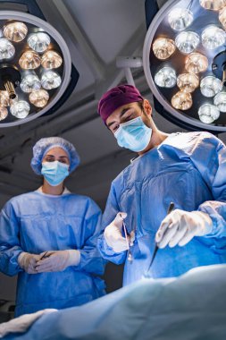 A surgeon performs an operation in a sterile operating room, with a surgical assistant observing.