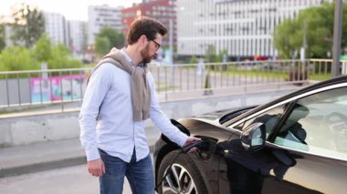 Bir adam gülümser ve elektrikli aracını şarj ederken başparmağını kaldırır, sürdürülebilir ulaşımı teşvik eder..
