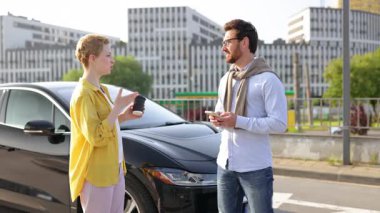 Bir adam ve bir kadın siyah elektrikli bir arabanın önünde el sıkışıyor, muhtemelen bir iş anlaşmasından sonra..