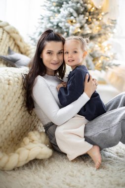 Bir anne ve küçük kızı, arka planda bir Noel ağacı ile kucaklaşarak hassas bir anı paylaşıyorlar..