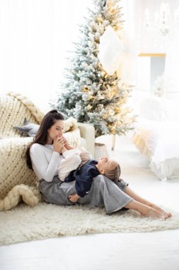 Bir anne ve çocuk, arka planda bir Noel ağacı ile sıcak ve şenlikli bir atmosfer yaratarak hassas bir anı paylaşıyor..