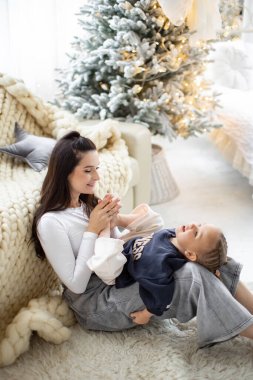 Bir anne ve çocuk, Noel ağacının önünde sıcak ve şenlikli bir atmosfer yaratarak neşeli bir anı paylaşırlar..