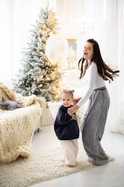 Neşeli bir anne ve kız Noel için dekore edilmiş, ışık ve mutlulukla dolu bir salonda dans ediyorlar..