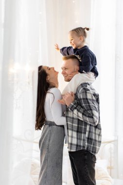 Üç kişilik neşeli bir aile, babalarının omuzlarına tünemiş bir çocukla yürek ısıtan bir anı paylaşır..