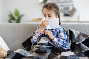 Battaniyeye sarılı genç bir kız kanepeye oturur ve burnunu silmek için mendil kullanır. Muhtemelen soğuk algınlığı ya da hastalıktan muzdariptir..