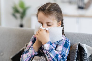 Örgülü genç bir kız, kanepede oturur, burnunu silmek için mendil kullanır, muhtemelen soğuk algınlığı ya da alerjiden muzdariptir..