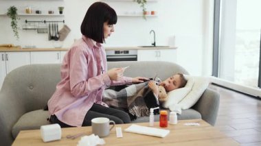 Endişeli bir anne, kanepede dinlenirken kızının ateşini ölçer..