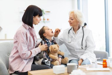 Bir doktor, genç bir kızın boğazını muayene etmek için dil bastırıcı kullanır. Annesi de klinikte muayene sırasında onu rahatlatır..