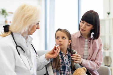 Endişeli bir anne, doktorların kızlarının ateşini termometreyle ölçtüğünü izler. Muhtemel sağlık kontrolü sırasında. Çocuk iyi görünmüyor..