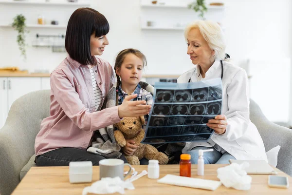 Bir doktor, oyuncak ayıyı sıcak bir ortamda tutan bir anneye ve kızına röntgen filmini açıklar. Olay yerinde bir masada tıbbi malzemeler var..