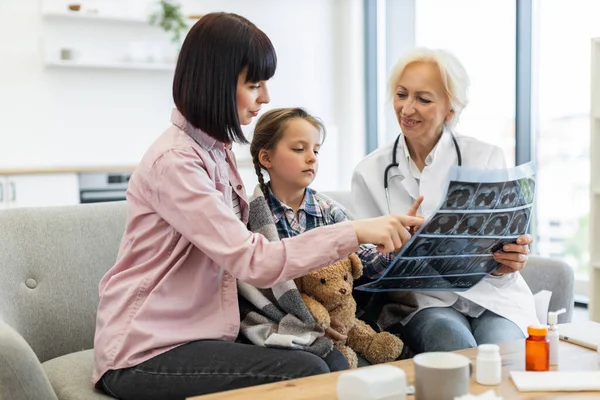 Bir doktor, elinde oyuncak ayıyla gezen bir anneye ve küçük kızına sonuçları açıklarken röntgene işaret ediyor..