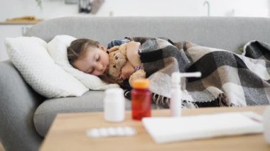 Genç bir kız kanepede uyur, oyuncak ayıyla kucaklaşır ve battaniyeyle kaplanır..