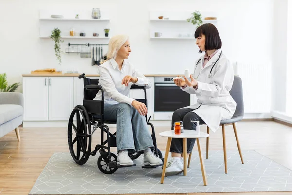 Bir doktor, ev ziyareti sırasında tekerlekli sandalyedeki yaşlı bir kadına tedavi ve destek öneriyor..