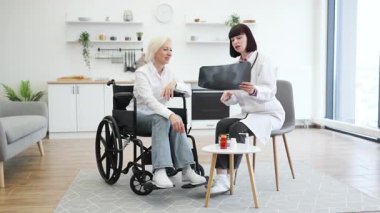 Doktor, tekerlekli sandalyedeki yaşlı bir hastaya röntgen filmini açıklar. Sahne iyi aydınlatılmış, modern bir ev ortamında geçiyor..