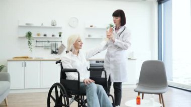 Kadın bir doktor, tekerlekli sandalyedeki yaşlı bir kadının kolunu muayene ediyor, muhtemelen sağlığını değerlendiriyor..