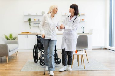 Doktor yaşlı bir kadına bastonuyla, tekerlekli sandalyesiyle, sağlık hizmetlerini ve desteklerini desteklemek için yardım eder..