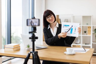 Masa başında gözlüklü beyaz bir kadın iş analizi ve büyüme hakkında blog yazıyor. İletişim işi eğilimleri, uzak iş eğitimi ve profesyonel kalkınma gibi kavramları yakalar.