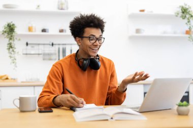 Gözlüklü genç bir adam telefon görüşmesinde gülümsüyor, not defterine not alıyor..