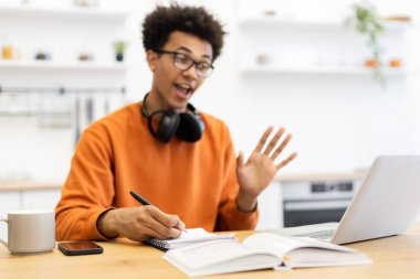 Gözlüklü genç bir adam ekranda el sallarken not alıyor..