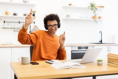Gözlüklü ve kulaklıklı neşeli bir adam evde dizüstü bilgisayarla çalışırken müziğin keyfini çıkarıyor..