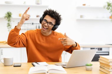 Kulaklıklı genç bir adam evde dizüstü bilgisayarla çalışırken gülümsüyor ve puanlar alıyor..