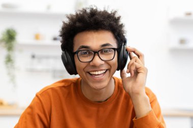 Gözlüklü genç bir adam kulaklık takarken geniş bir gülümseme takıyor, içeride müzik dinlemekten hoşlanıyor..