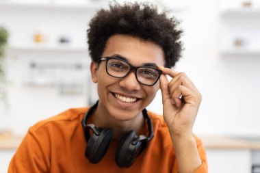 Gözlüklü genç bir adam kameraya gülümsüyor, kulaklıkları boynunda..