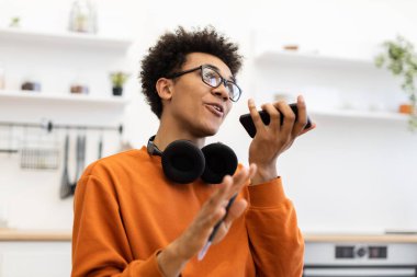 Gözlüklü genç bir adam telefonuyla konuşuyor, elleriyle işaret ediyor..