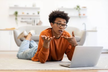 Gözlüklü genç bir adam dizüstü bilgisayarıyla video görüşmesi yapıyor ve elleriyle işaret ediyor..