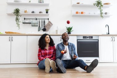 Mutlu bir çift, modern bir mutfakta yerde oturmuş elmalarla hokkabazlık yapıyor..