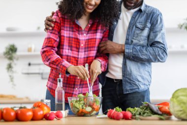 Gülümseyen bir çift, parlak bir mutfakta taze bir salata hazırlar. Birlikte olmanın ve sağlıklı beslenmenin tadını çıkarırlar..