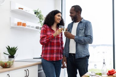 Gülümseyen bir çift şampanya kadehlerini modern mutfak ortamında tokuşturur..