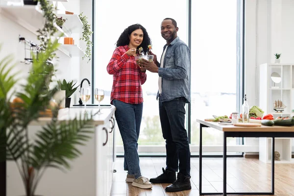 Gülümseyen bir çift birlikte salata hazırlar. Parlak, modern bir mutfakta, sağlıklı bir yemeğin tadını çıkarırlar..