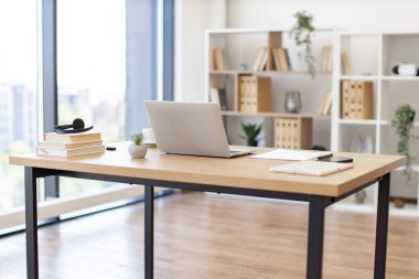 A laptop, books, and other items sit on a desk in a bright, modern office setting